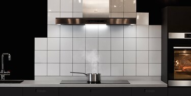 Tilbereding av laks på en induksjonskoketopp mens kjøkkenventilatoren håndterer dampavtrekket