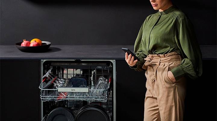 Kvinne i en grønn bluse som bruker en telefon ved siden av en oppvaskmaskin