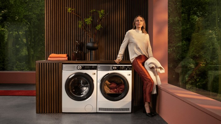 En kvinne står ved en tørketormmel og venter på at vasken skal bli tørr.