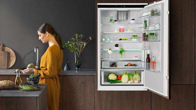 Kvinne som står på et kjøkken med en åpen kjøleskapsdør.