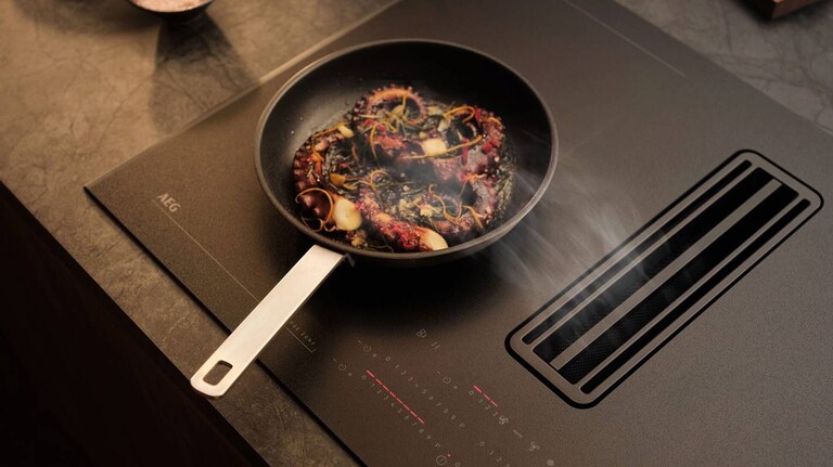 Mat tilberedes in en stekepanne på en induksjonstopp med integrert ventilator.