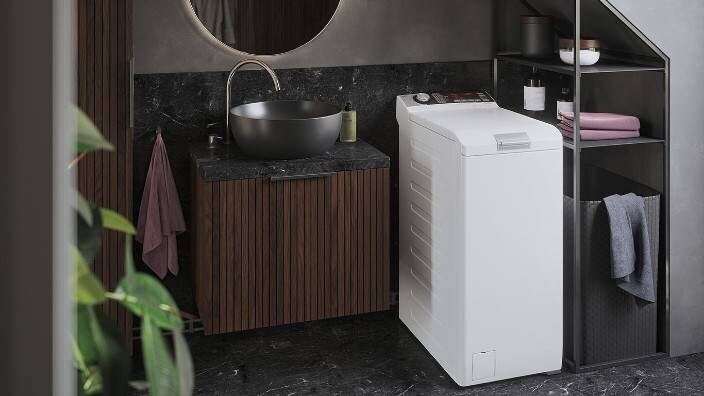 En toppmatet vaskemaskin som står på et mindre vaskerom.
