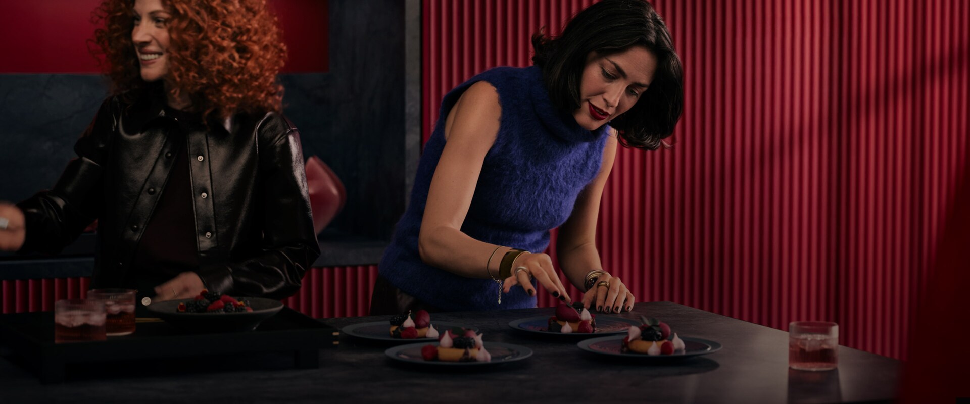 To kvinner tilbereder dessert på en mørk kjøkkenøy.