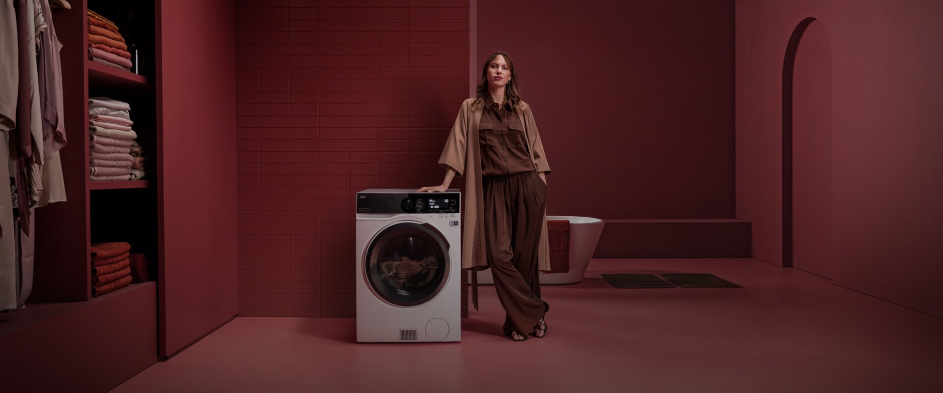 En kvinne som står ved siden av en frittstående vaskemaskin med tørketrommel i et rødt rom.