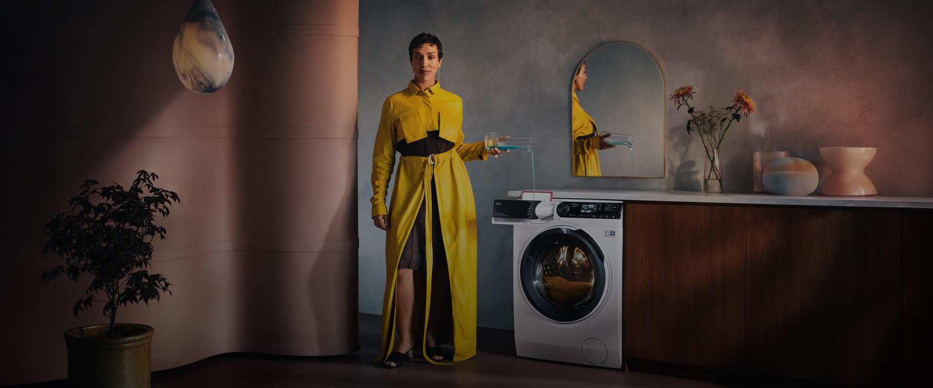 En kvinne i gul kjole heller vaskemiddel i en vaskemaskin.