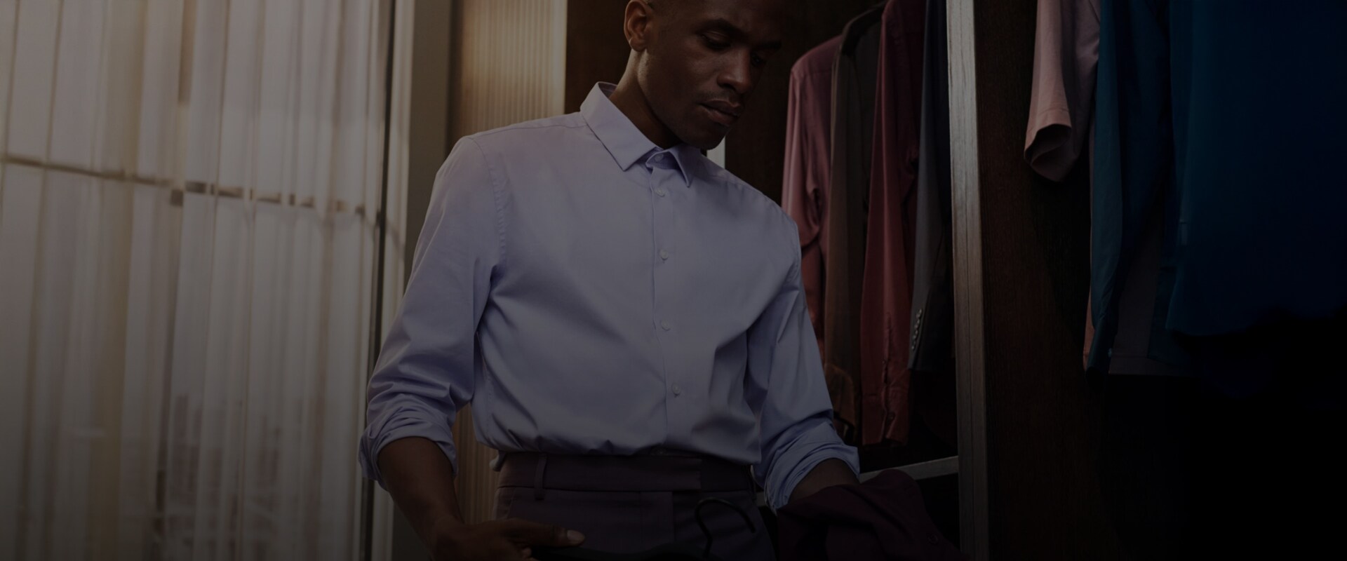 En mann i blå skjorte står ved en garderobe og velger klær.